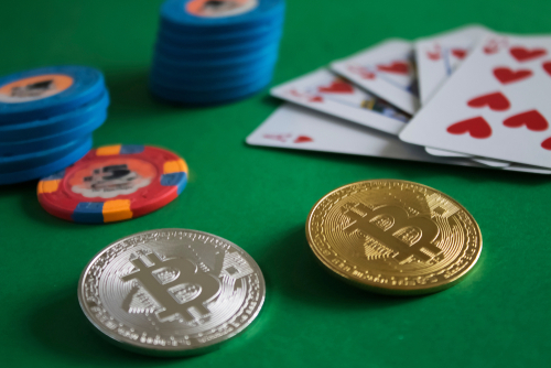 deux bitcoin posés sur une table de jeu avec des jetons de casino et un jeu de cartes